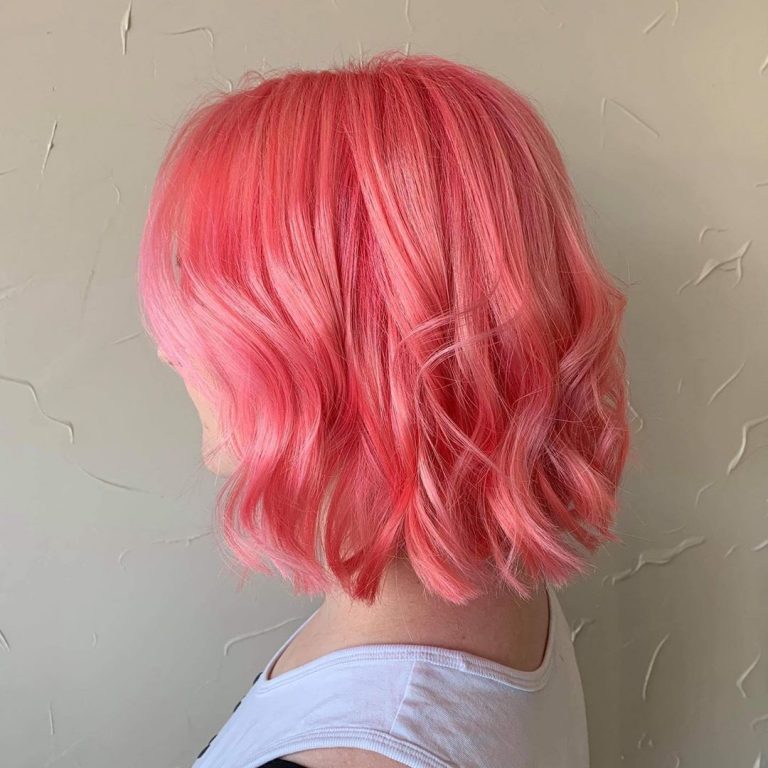 A woman with pink hair is looking at the wall.