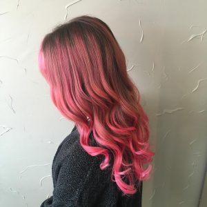 A woman with pink hair is standing in front of a wall.
